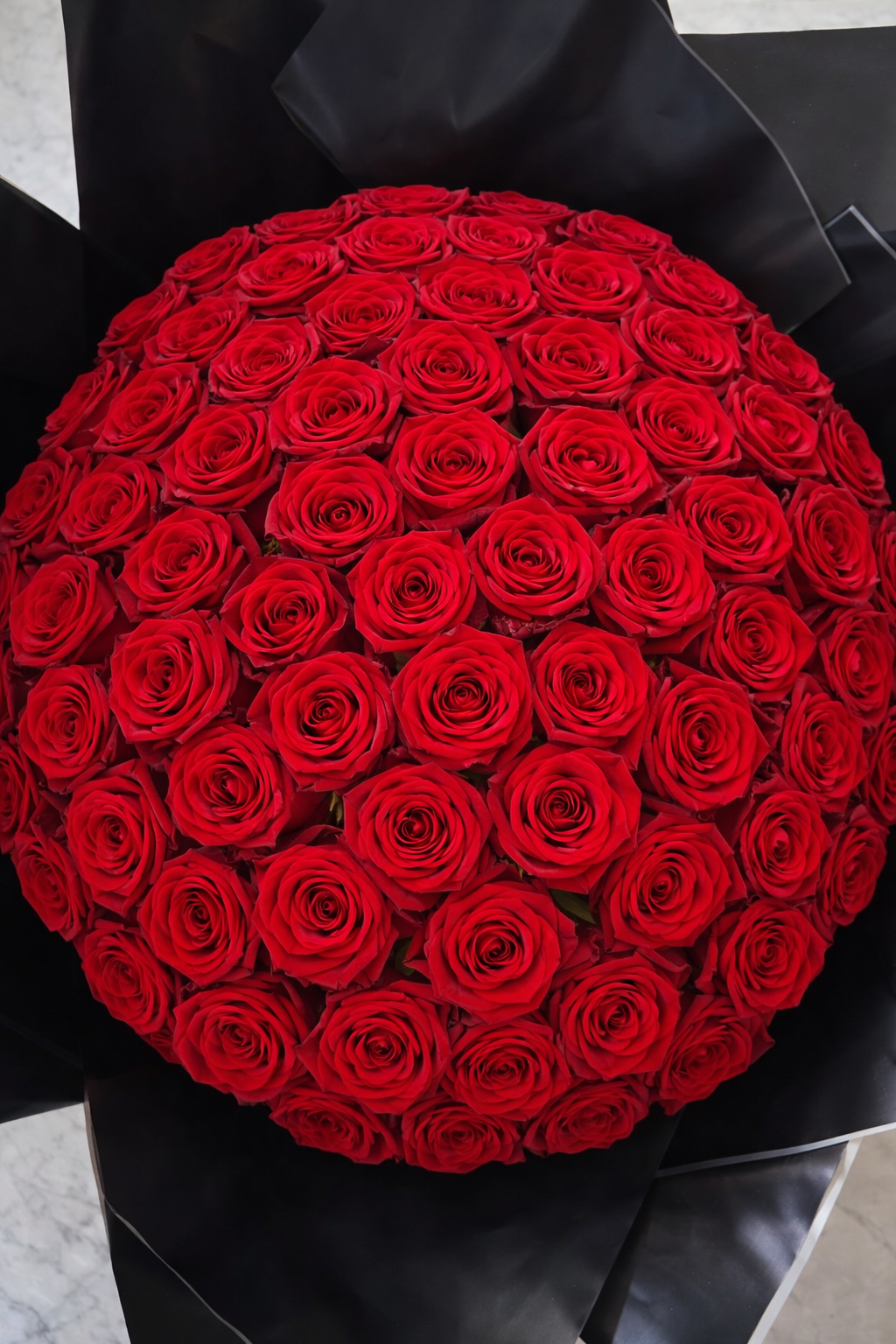 Bouquet of red roses wrapped in black paper on a light grey surface