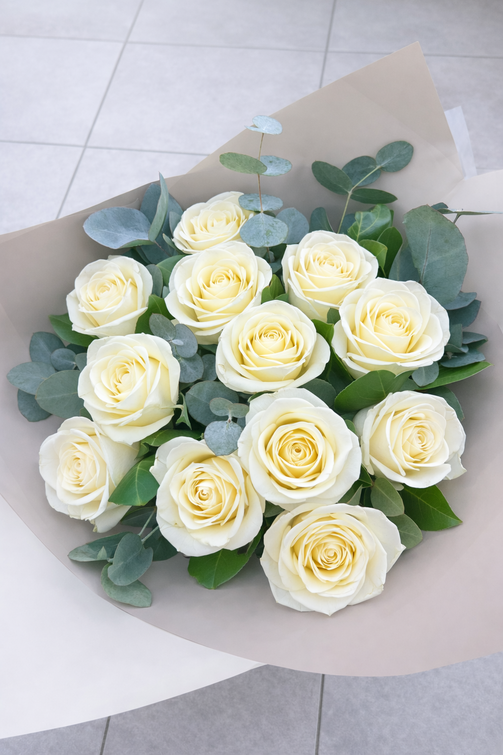 Bouquet of white roses with green leaves on a light grey surface