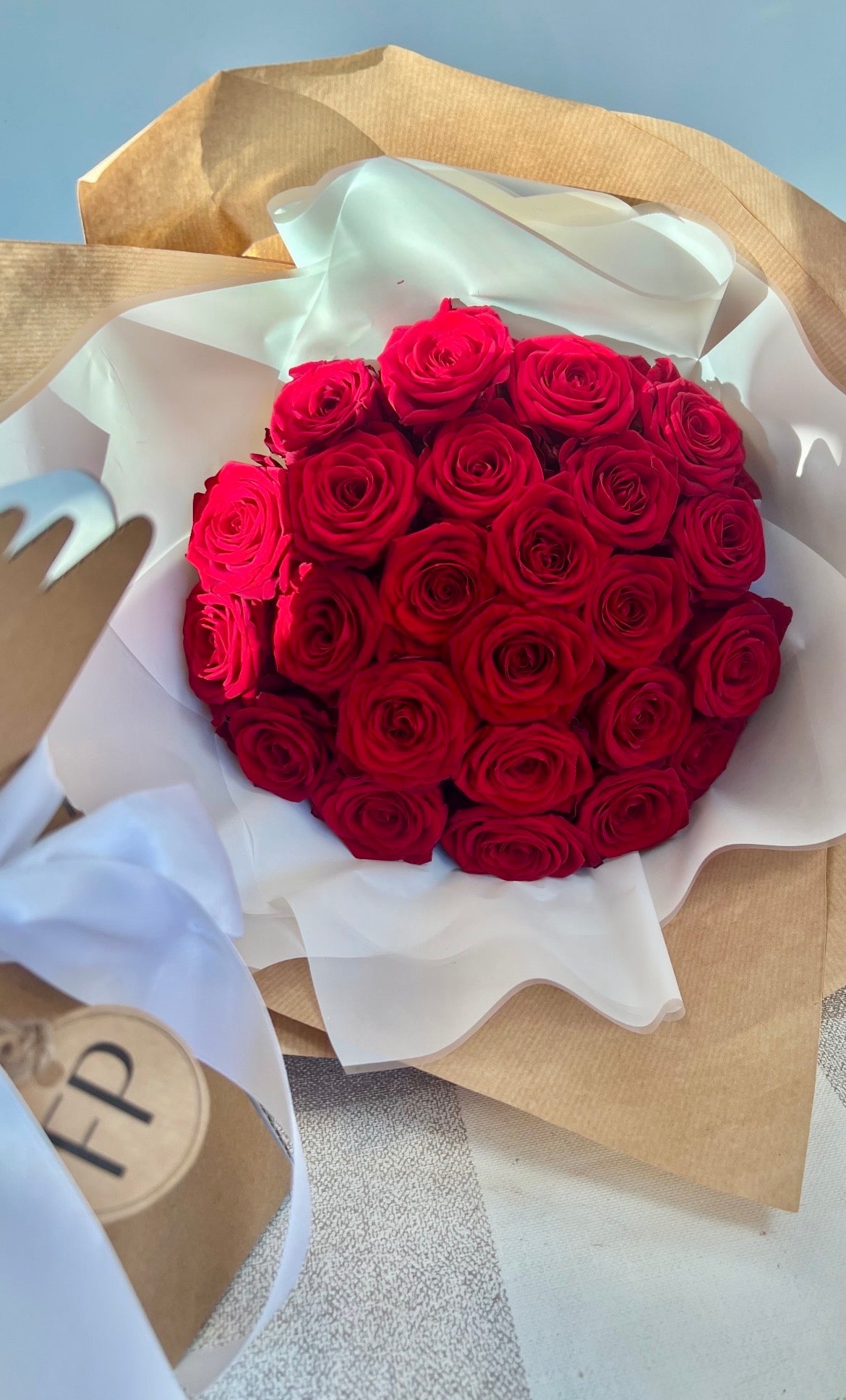 Bouquet of red roses wrapped in brown paper with a white ribbon on a light grey background.