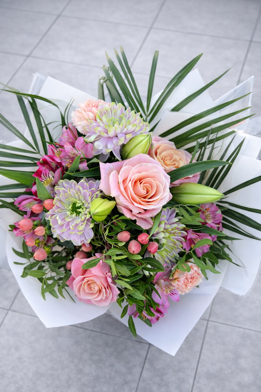 Bouquet of flowers with pink and green elements on a gray floor.