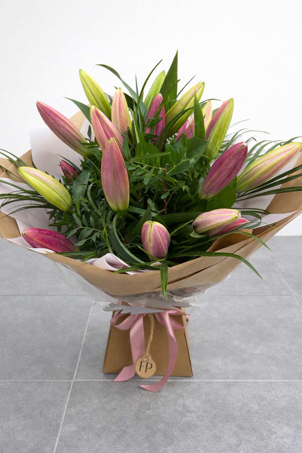 Bouquet of pink and green lilies with a brown paper wrap on a gray surface