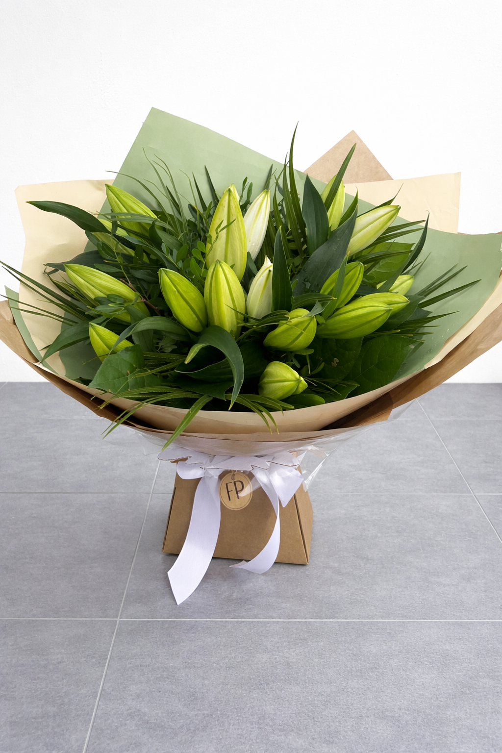 Bouquet of white lilies wrapped in brown paper with a white ribbon on a grey surface.