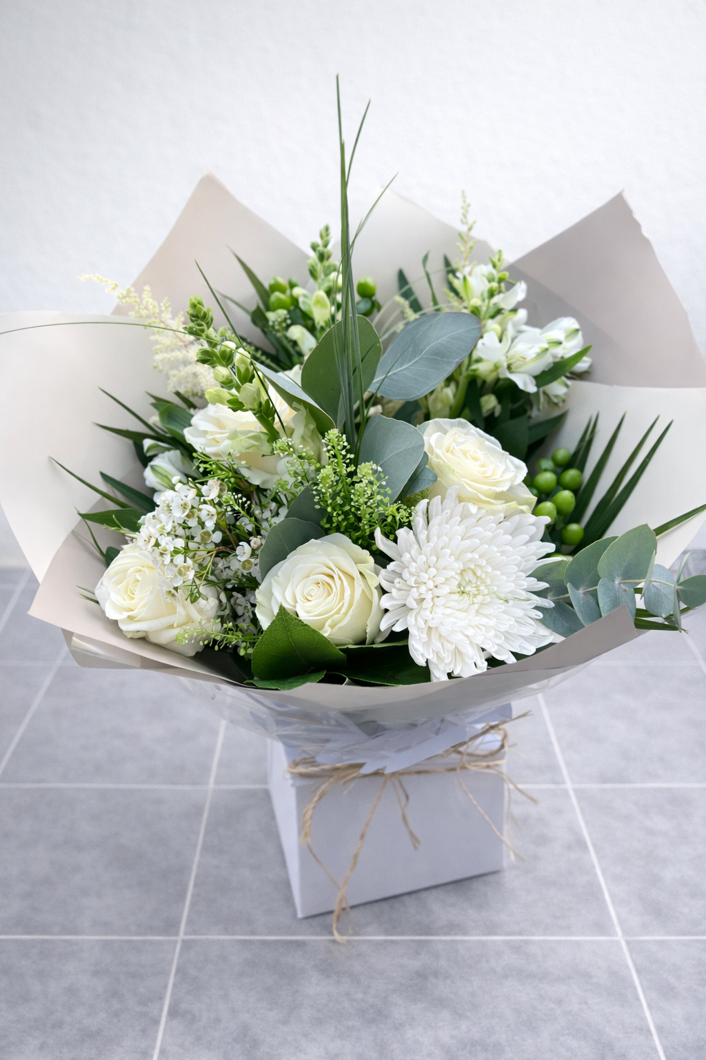 Bouquet of white and green flowers wrapped in paper on a tiled floor.